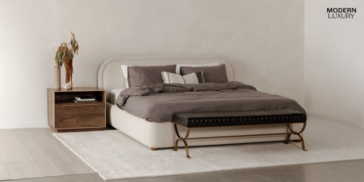 A clean and elegant guest bedroom with a white upholstered bed, gray bedding, wooden nightstand, and a bench at the foot of the bed.